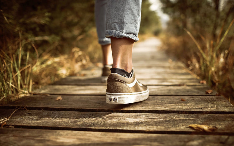 Person walking on wooden path wearing casual sneakers, showcasing shoe hygiene and comfort in natural surroundings.